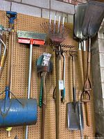 Photo of various garden tools hanging on a pegboard including shovels, rakes, hoes, and trimmers.