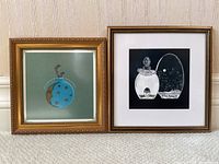 Two framed vintage gouache paintings featuring perfume bottles, one blue with stars and crescent moon, and one black and white with two bottles