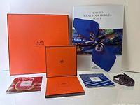 Group shot: two Hermès boxes, ribbon and all booklets arranged on white background