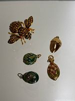 Photo showing Joan Rivers amber rhinestone bee brooch with green eyes alongside four Faberge egg inspired charms including floral cloisonné designs and an acorn.