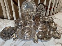 Overview of all silverplate serving pieces arranged on marble countertop