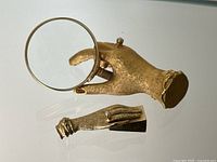 Large gilt metal hand paperweight holding magnifier next to small hand pencil sharpener