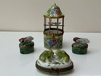All four enamel trinket boxes arranged together: one oval frog box, two oval bee boxes, one birdcage box