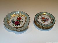 Photo showing one shell-shaped serving dish and stack of six vintage floral porcelain plates with gold leaf accents