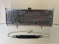 Front view of floral embossed aluminum clutch with detachable chain strap laid out