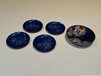 Five copper dishes: one larger colorful enamel dish and four smaller cobalt blue floral dishes arranged on white surface