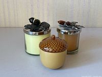 Three acorn themed candles displayed with decorative lids and ceramic acorn container.