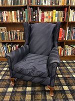 Navy blue wingback chair with down cushion shown from front and slight angle, highlighting upholstery and wooden leg detail.