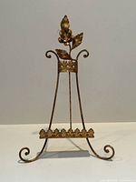 Front view of ornate Italian gilt metal art easel showing decorative floral motif and curled feet base.