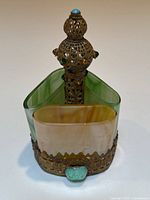 Front view showing triangular art glass compartments and ornate metal handle topped with a turquoise colored gem.