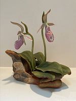 Front and side view of the porcelain Lady Slipper Orchid sculpture showing two pink and white flowers, green leaves, and woody base.