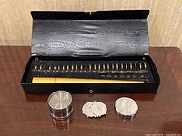 Black hinged storage box open showing gold-colored mandrel and brass gauge rings labeled US sizes 1 through 15 with half sizes
