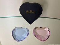 Two Rosenthal heart-shaped crystal paperweights displayed on glass table with original black Rosenthal box in the background.