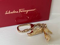 Gold-tone Salvatore Ferragamo keychain with two shoe charms, placed next to a red box with Ferragamo logo.