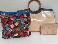Two vintage handbags displayed side by side, including a multicolor floral leather bag and a cream butterfly-patterned leather handbag with bamboo handles and matching clutch.