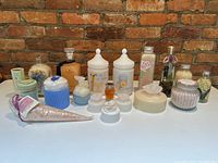 Overall view of 18 assorted bath and vanity jars and bottles on white surface against brick wall