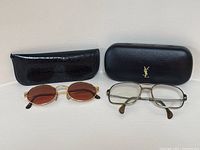 Two pairs of glasses with cases: black YSL case on right, black croc-embossed case on left