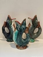 Group view of three glazed ceramic fish jugs in varying colors