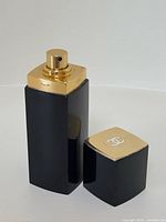 Open black and gold Chanel No. 5 perfume bottle showing spray nozzle and removed cap with white Chanel logo on top.