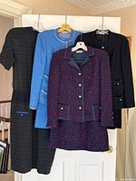 Four garments hung on hangers against white background: black polka dot dress, light blue suit, purple tweed suit, black suit.