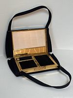 Black satin purse open flat showing full vanity layout with compartments and mirror.