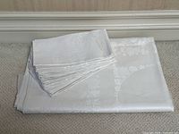 Folded white damask tablecloth with matching folded napkins on a carpeted floor