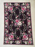 Full view of vintage needlepoint rug displaying overall floral design and border on dark background.