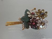 Front view showing gold-tone metal brooch with multicolor rhinestone and enamel flowers and carved green leaves