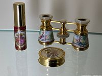 Three-piece lot shown on glass tabletop: opera glasses, porcelain atomizer, floral pill box
