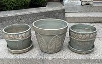 Photo of three green vintage garden planters with matching clay trays arranged on concrete steps, showing overall condition and size.
