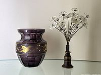 Front view of purple crystal vase and metal/glass flower bouquet on glass table against white wall