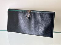 Front exterior view showing black pebbled leather and gold-tone hand-shaped clasp