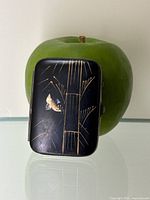 Full view of match holder box shown in front of a green apple for scale, measuring approximately 1.75 by 2.25 inches.