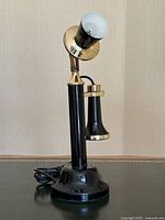 Front view showing the lamp shaped like an antique telephone with black metal base and stem, brass accents, and bulb shade on top.