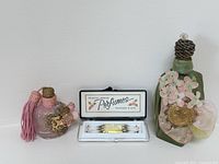 Three items: two decorative vintage perfume bottles and a cased sampler set of miniature perfume vials. Items shown together on white background.