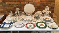 Wide shot of entire lot on white table against brick wall showing mixed porcelain and glass items