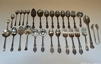 Full layout of all 29 vintage silver plated serving utensils including spoons, forks, ladles, and tongs in Birks Kings Primrose pattern on a white surface.