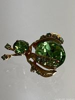 Close-up front view of the insect-shaped brooch showing large green faceted stone on body and smaller rhinestones on wings and antennae.