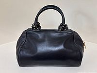 Front view of black leather handbag showing smooth exterior and handle attachment