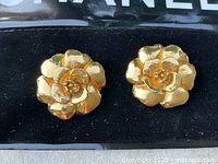 Pair of Chanel camellia clip-on earrings on black velvet.