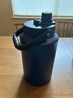 Full view of the navy blue stainless steel beverage keg sitting on a wooden table with the handle raised vertically.