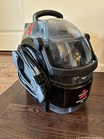 Front and side view of Bissell SpotClean Pro portable carpet cleaner showing the transparent water tanks and power cord wrapped on the side