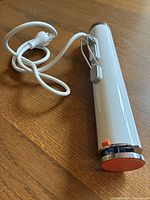 White and stainless steel slim cylindrical sous vide immersion circulator with attached power cord laid on wooden table.