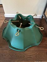 Green plastic Christmas tree stand with four metal screws with looped handles.