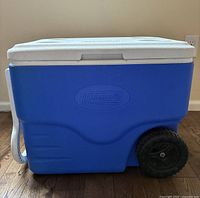 Side view of blue Coleman cooler showing white lid, black wheel, and carry handle.