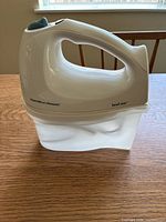 Side view of the white Hamilton Beach hand mixer showing ergonomic handle with brand and bowl rest label.