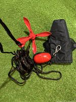 Red folding anchor with attached black and red rope, red float and black carrying pouch on green grass.