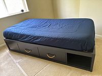 Side view of the navy twin bed showing three built-in drawers with rope handles and an open shelf under the navy fitted bed sheet.