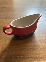 Side view showing red exterior and cream interior of the gravy boat, handle and pouring spout visible.