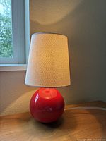 Close-up photo of the lamp showing the red spherical base and beige fabric lampshade with a light stain.